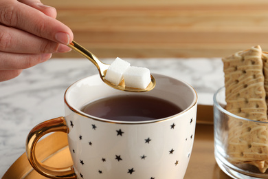 Woman adding refined sugar cubes to aromatic tea at table, closeup
