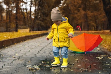 Photo of Cute little girl walking in puddle near colorful umbrella outdoors