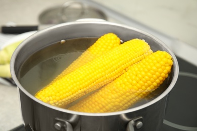 Photo of Pot with boiling corn cobs in kitchen, closeup