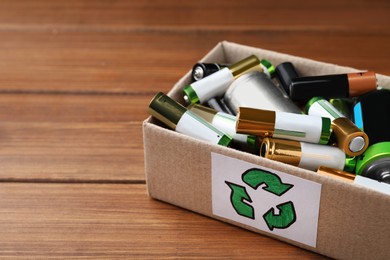 Image of Used batteries in cardboard box with recycling symbol on wooden table, closeup. Space for text