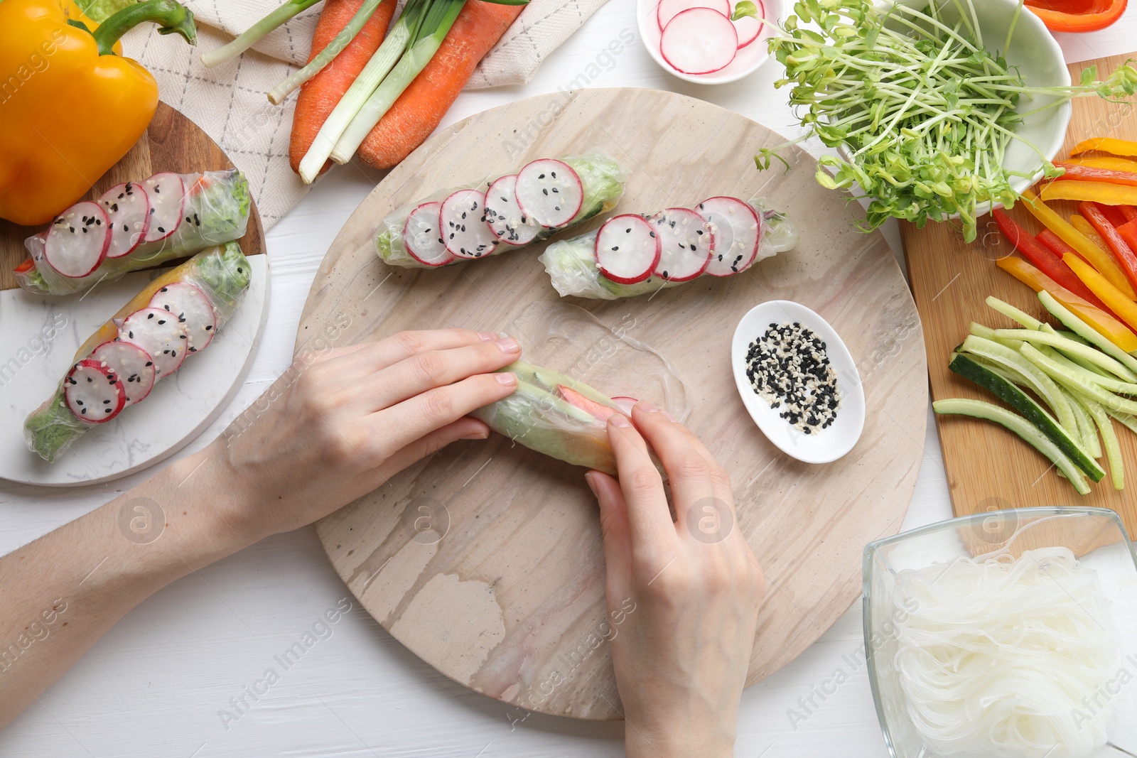 Photo of Woman wrapping spring roll at white wooden table with products, top view