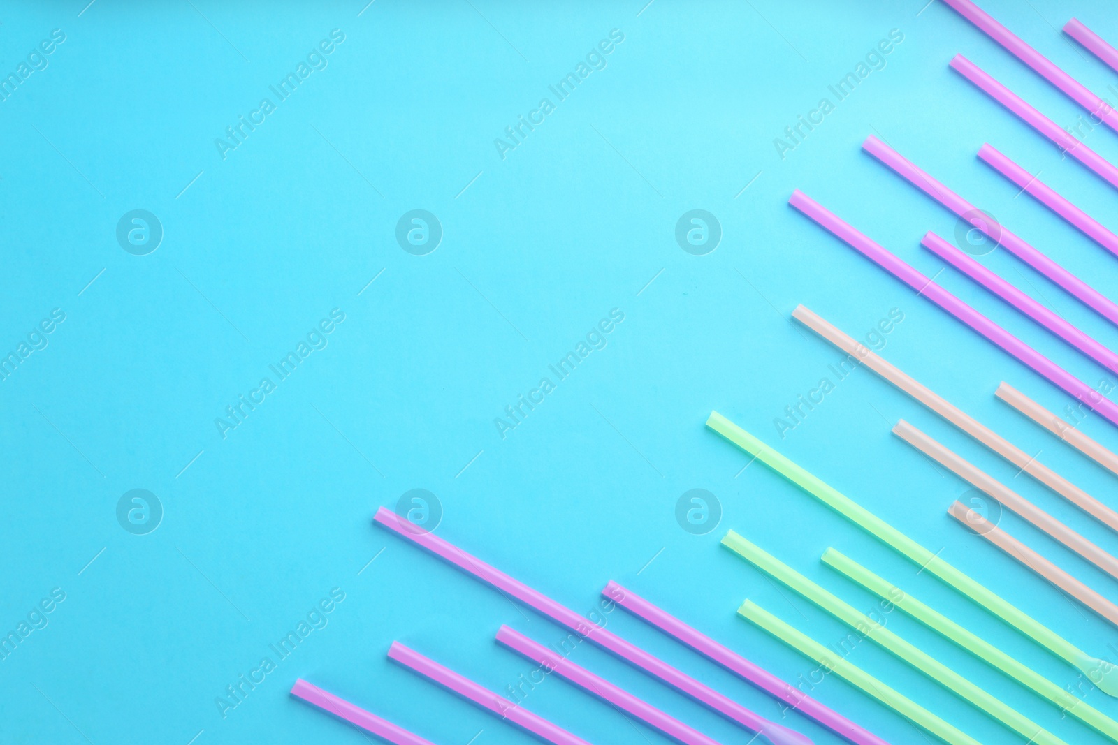 Photo of Colorful plastic drinking straws on light blue background, flat lay. Space for text