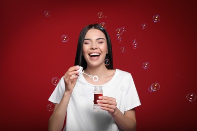 Young woman having fun with soap bubbles on red background