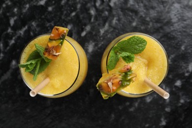 Photo of Tasty pineapple smoothie in glasses on black textured table, top view