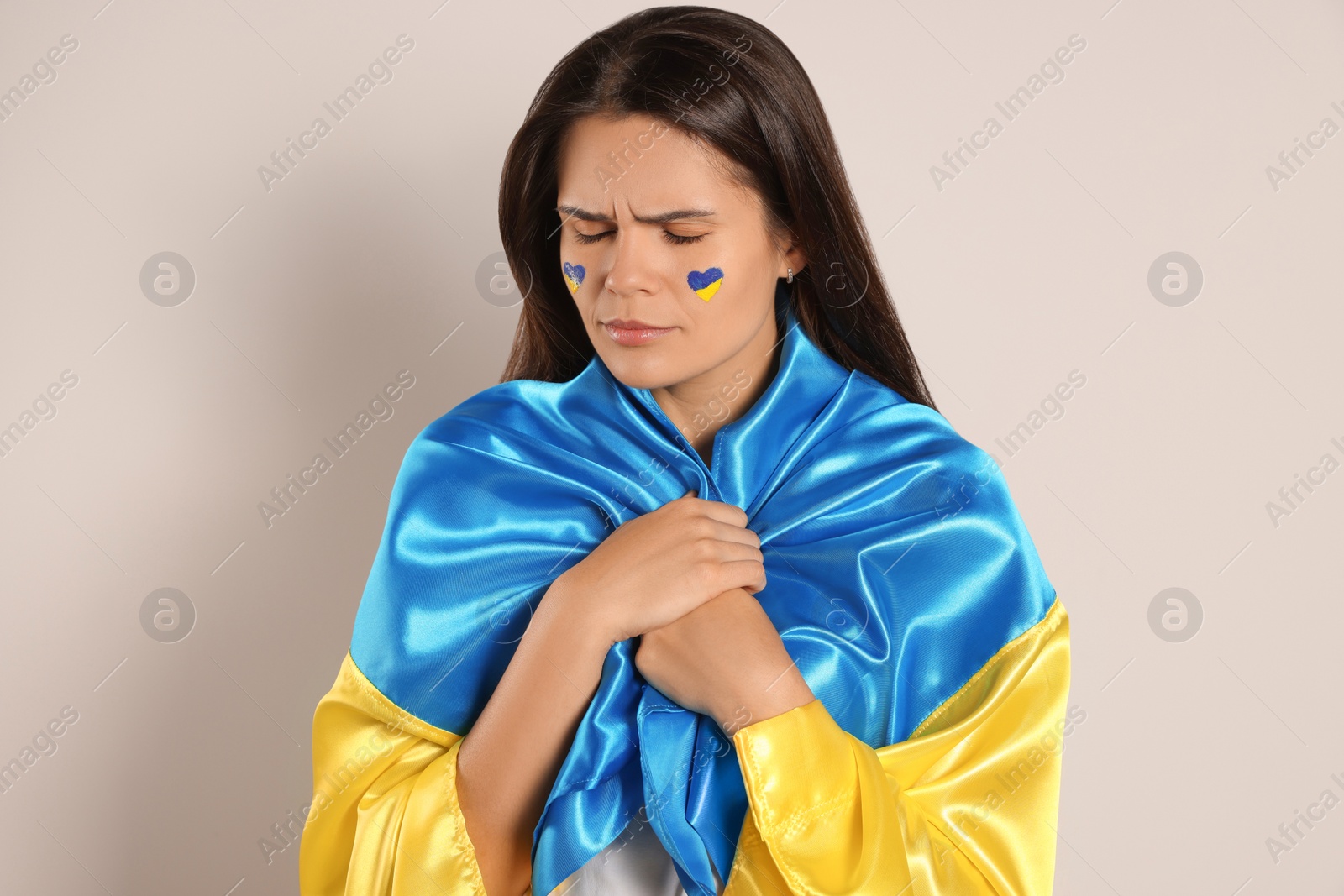 Photo of Sad young woman with face paint and Ukrainian flag on beige background