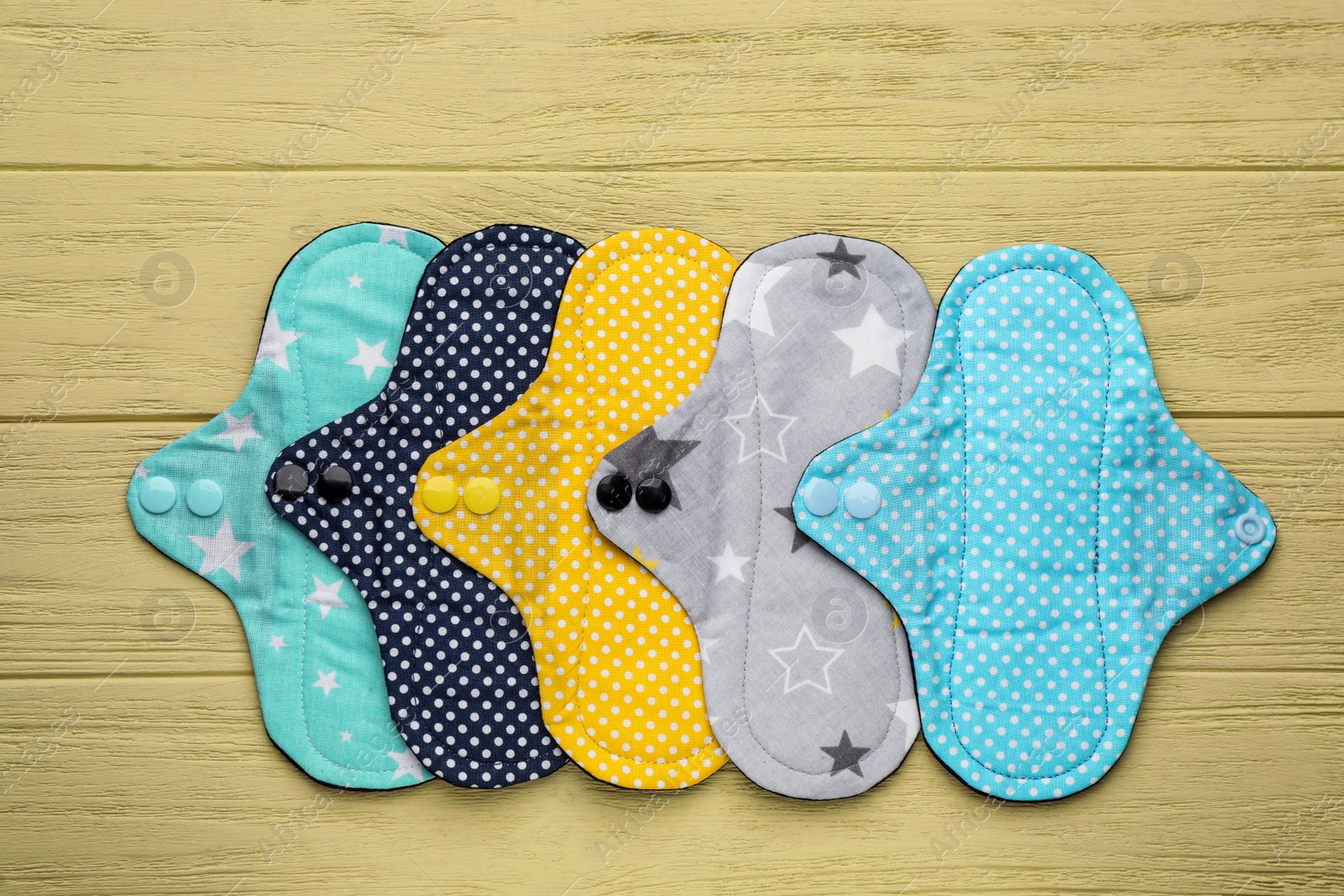Photo of Many reusable cloth menstrual pads on yellow wooden table, flat lay