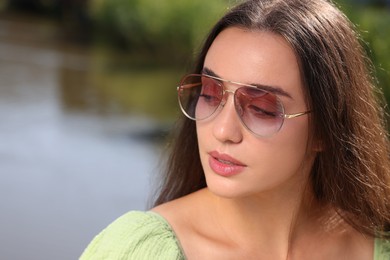 Beautiful woman in sunglasses near river, space for text