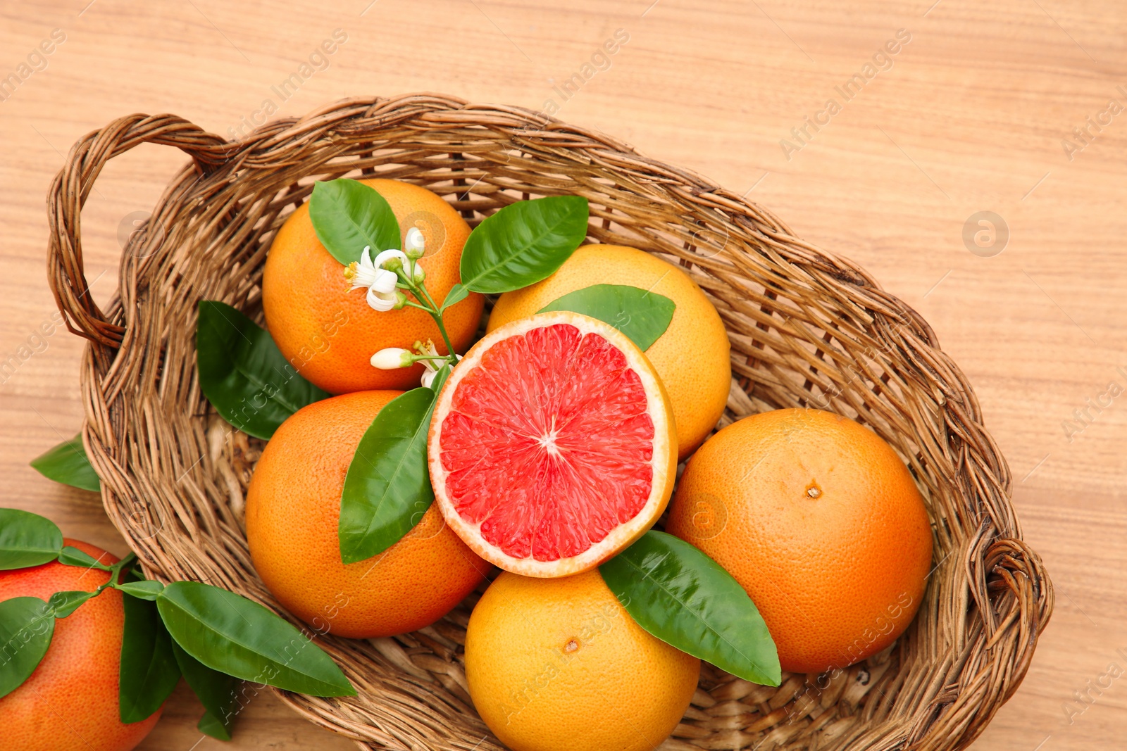 Photo of Wicker basket with fresh ripe grapefruits and green leaves on wooden table, top view