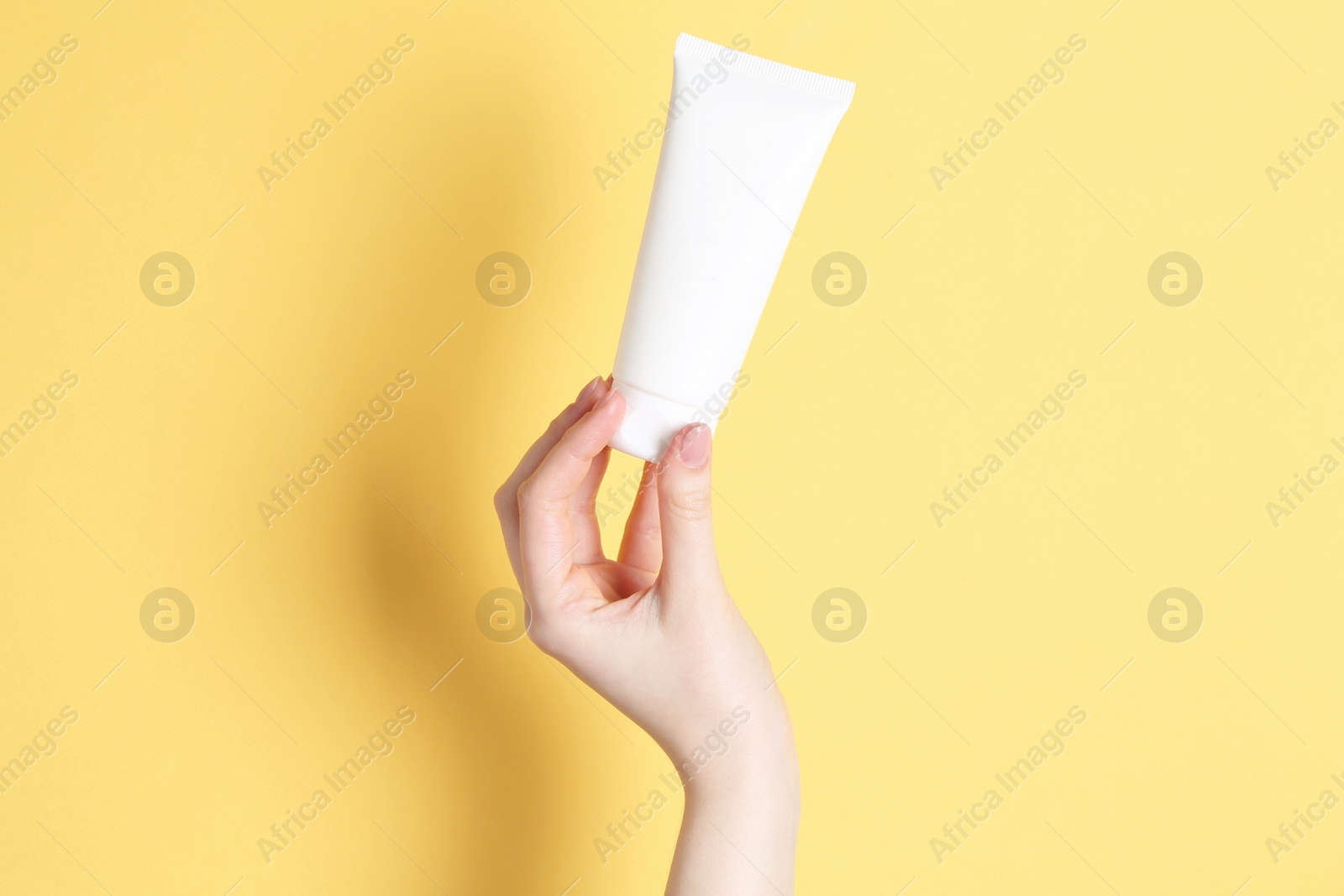 Photo of Woman holding tube of cream on yellow background, closeup