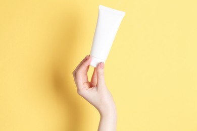 Photo of Woman holding tube of cream on yellow background, closeup