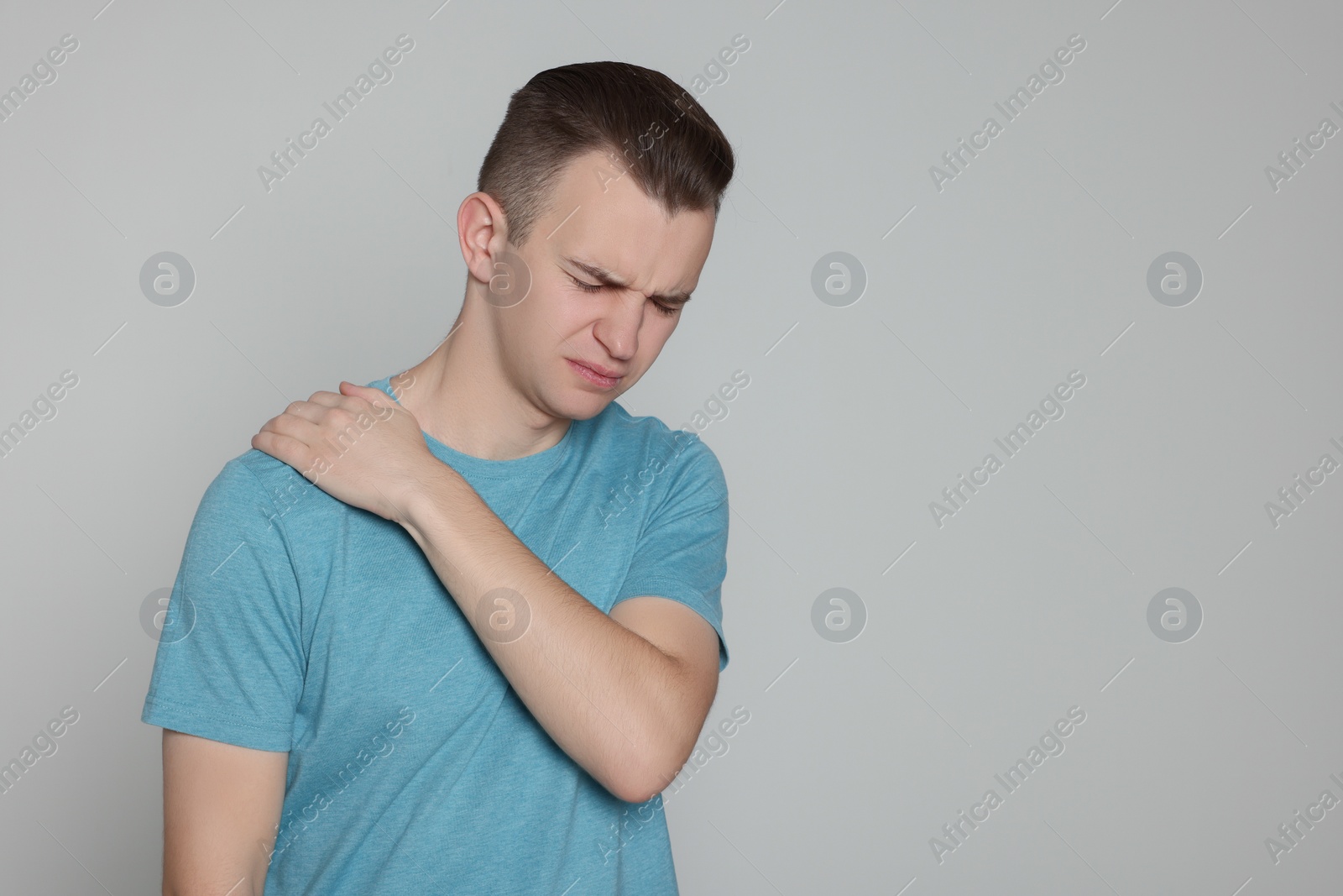 Photo of Young man suffering from pain in his shoulder on light grey background, space for text. Arthritis symptoms