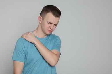 Young man suffering from pain in his shoulder on light grey background, space for text. Arthritis symptoms