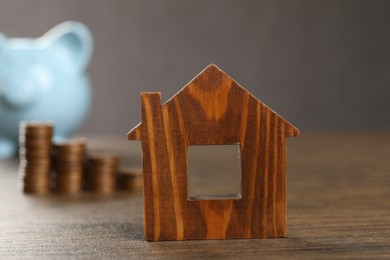 Photo of House model, piggy bank and stacked coins on wooden table, selective focus