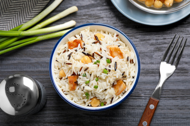 Photo of Delicious rice pilaf with chicken served on black wooden table, flat lay