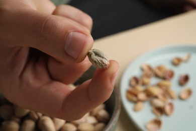 Woman holding tasty peeled pistachio nut over bowl, closeup. Space for text