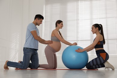 Photo of Pregnant woman and her husband working with trainer in gym. Preparation for child birth