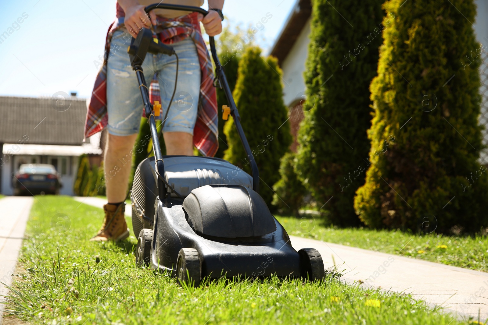 Photo of Man cutting green grass with lawn mower on backyard, closeup