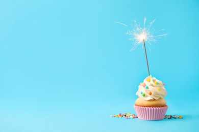 Photo of Birthday cupcake with sparkler on light blue background. Space for text