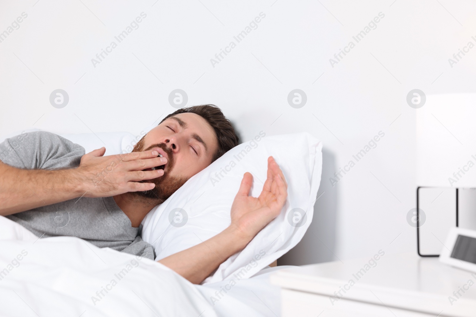 Photo of Handsome man yawning while lying on pillow in bed at home