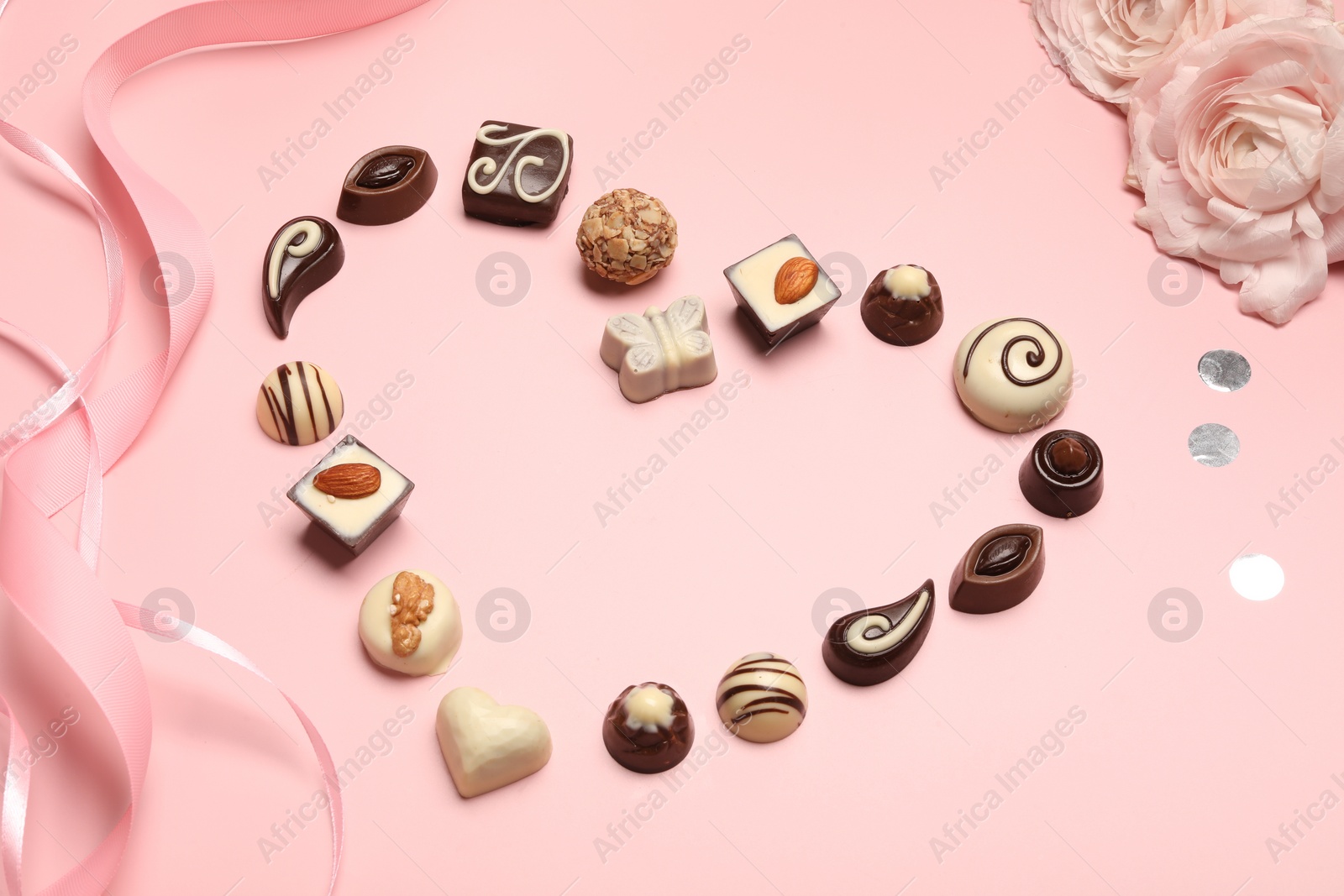 Photo of Heart made with delicious chocolate candies on light pink background