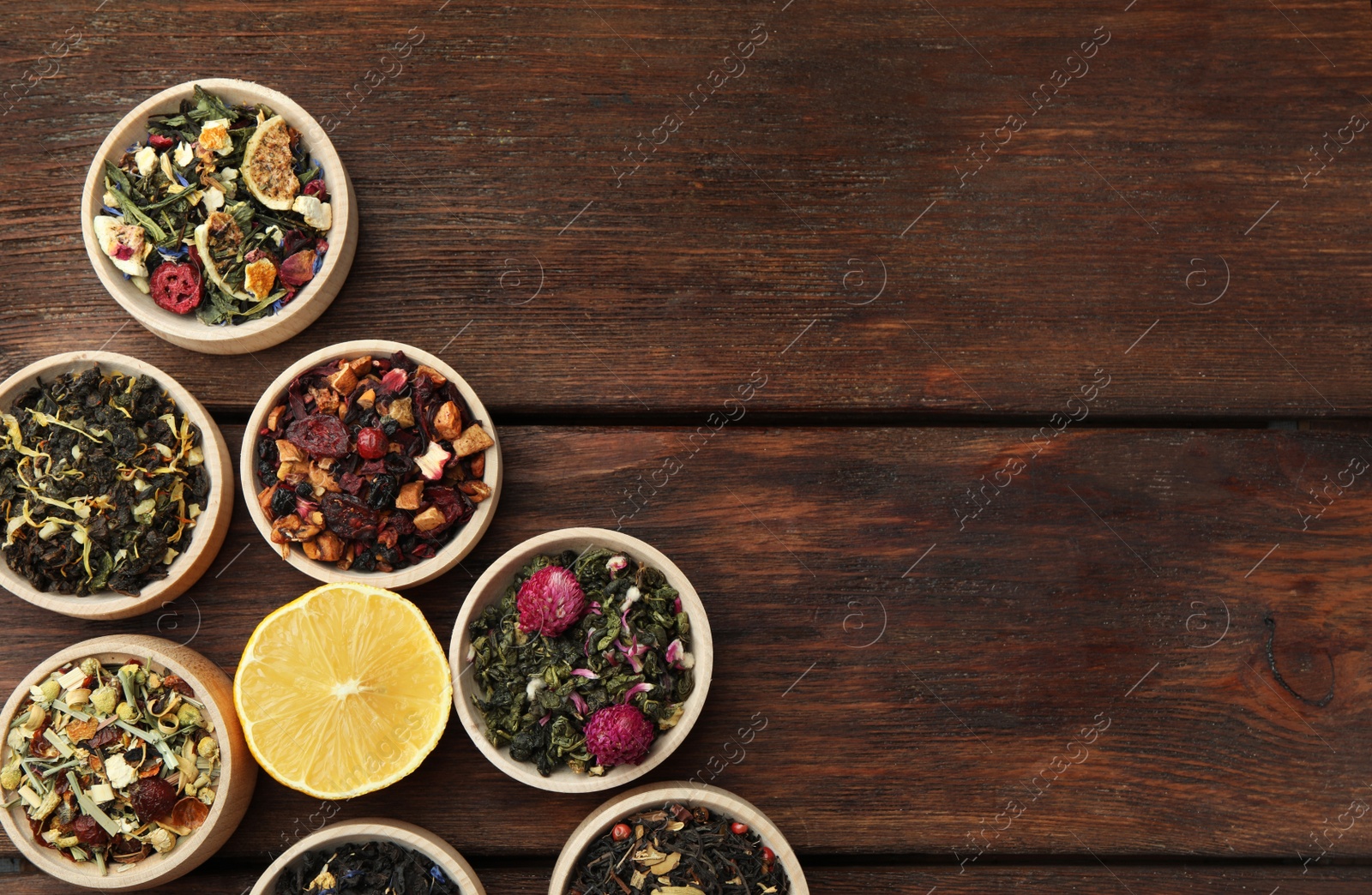 Photo of Different kinds of dry herbal tea in bowls on wooden table, flat lay. Space for text