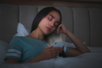 Photo of Young woman with nomophobia sleeping with smartphone in bed at night
