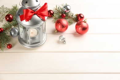 Photo of Christmas lantern with burning candle and festive decor on white wooden table. Space for text