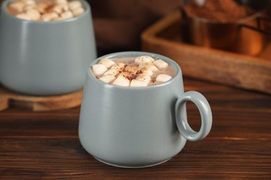 Photo of Cups of aromatic hot chocolate with marshmallows and cocoa powder on wooden table, closeup