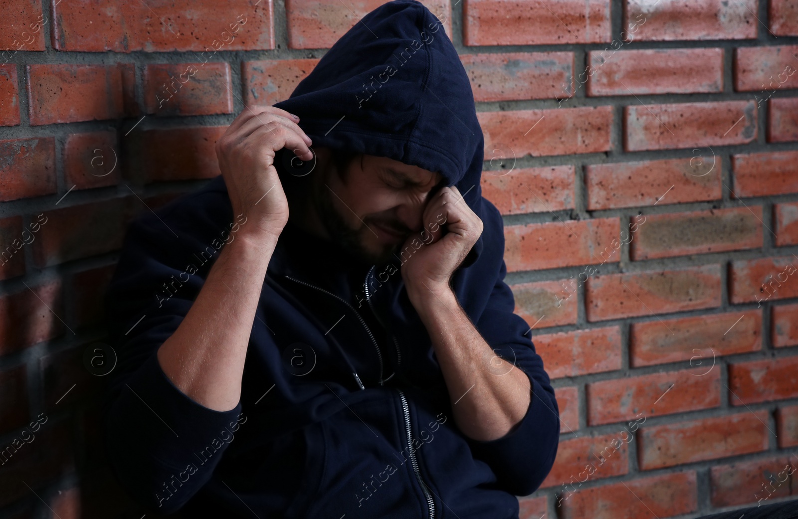 Photo of Young addicted man sitting near brick wall after using drugs