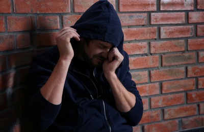 Photo of Young addicted man sitting near brick wall after using drugs