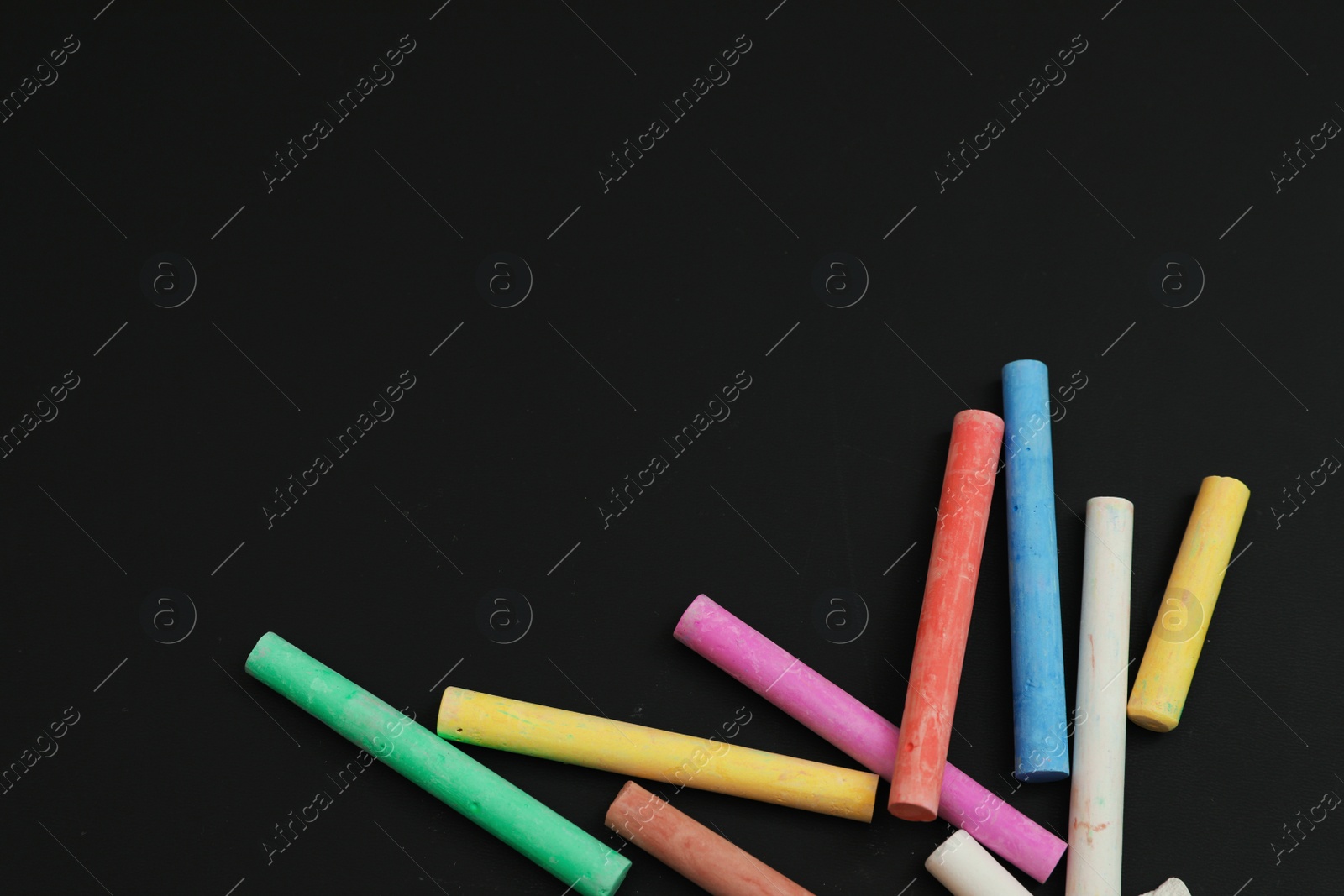 Photo of Colorful chalks on black board, flat lay. Space for text