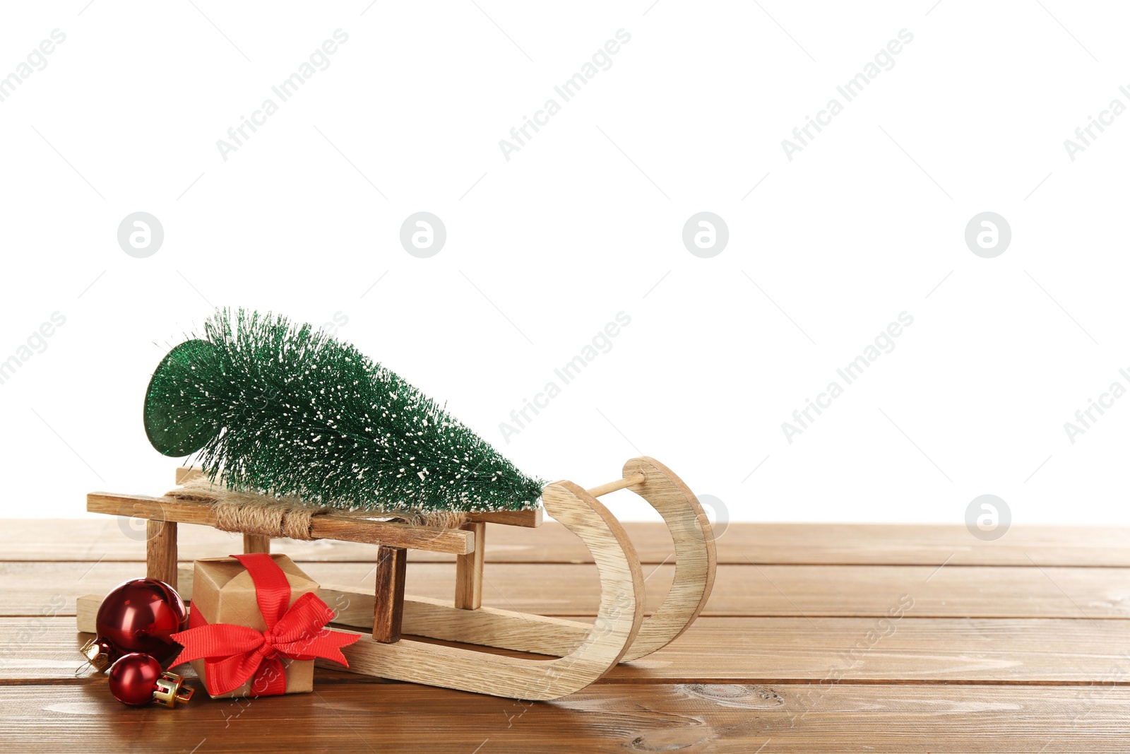 Photo of Small sleigh with decorative fir tree, gift box and Christmas balls on wooden table. Space for text