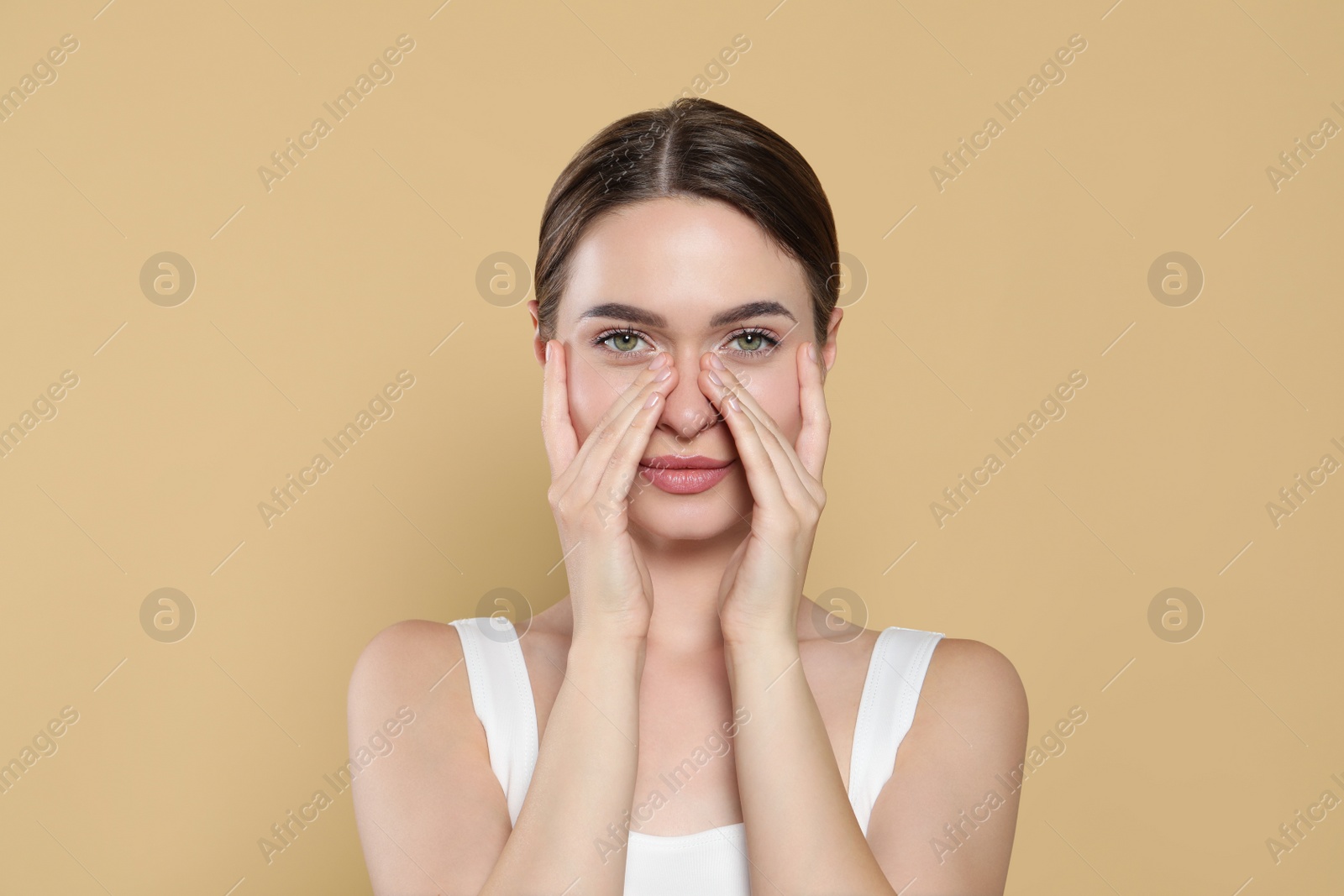 Photo of Young woman applying cream under eyes on beige background