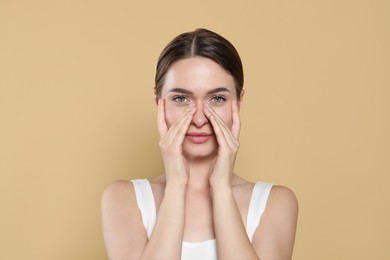 Photo of Young woman applying cream under eyes on beige background