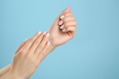 Photo of Woman with white polish on nails against light blue background, closeup. Space for text