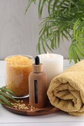 Photo of Spa composition. Bottle of cosmetic product, sea salt, burning candle and towel on white table