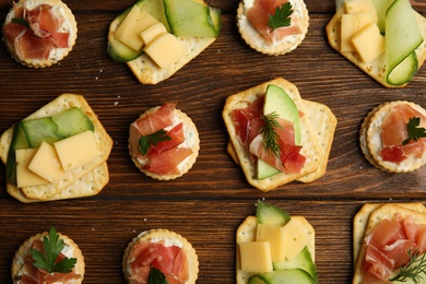 Photo of Different snacks with salted crackers on wooden table, flat lay