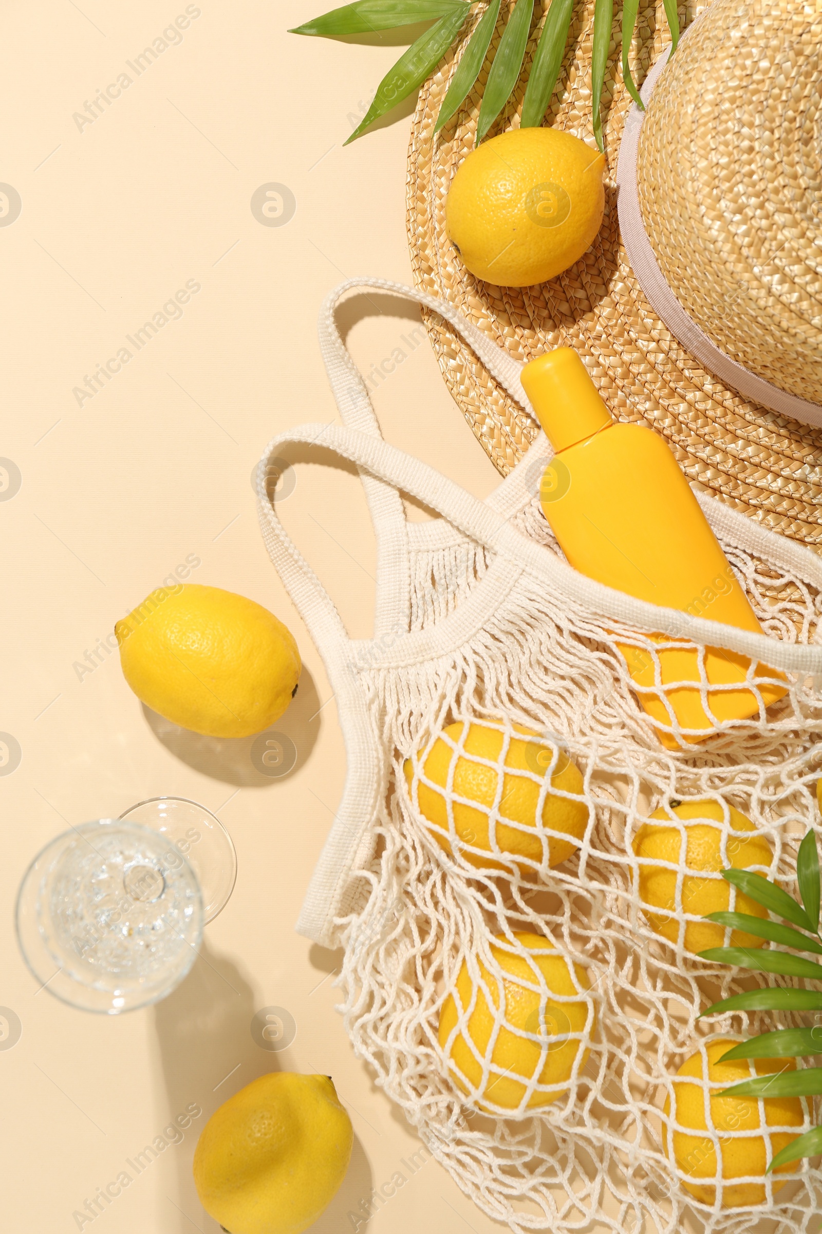 Photo of Fresh lemons, beach accessories in string bag and glass of drink on beige background, flat lay
