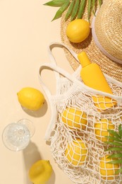Fresh lemons, beach accessories in string bag and glass of drink on beige background, flat lay