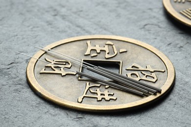 Photo of Acupuncture needles and Chinese coin on grey textured table, closeup
