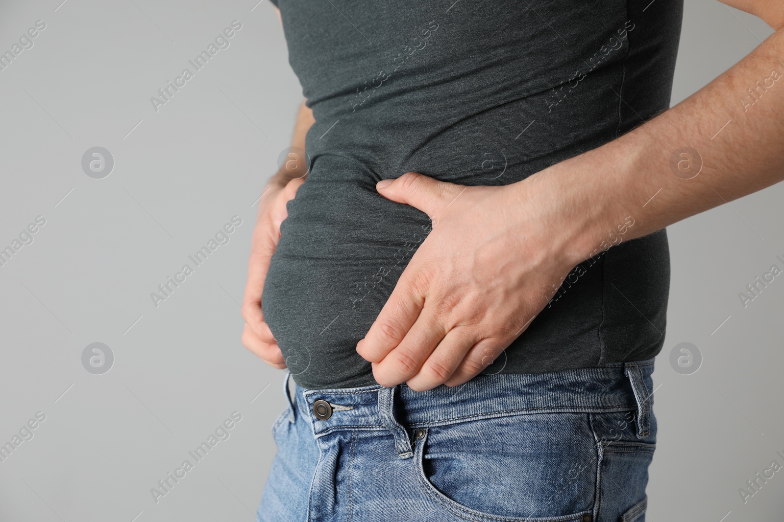 Photo of Overweight man in tight tshirt and jeans on light grey background, closeup. Space for text