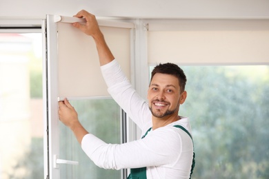 Man in uniform installing roller window blind indoors