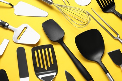 Photo of Different spatulas and other kitchen utensils on yellow background, closeup