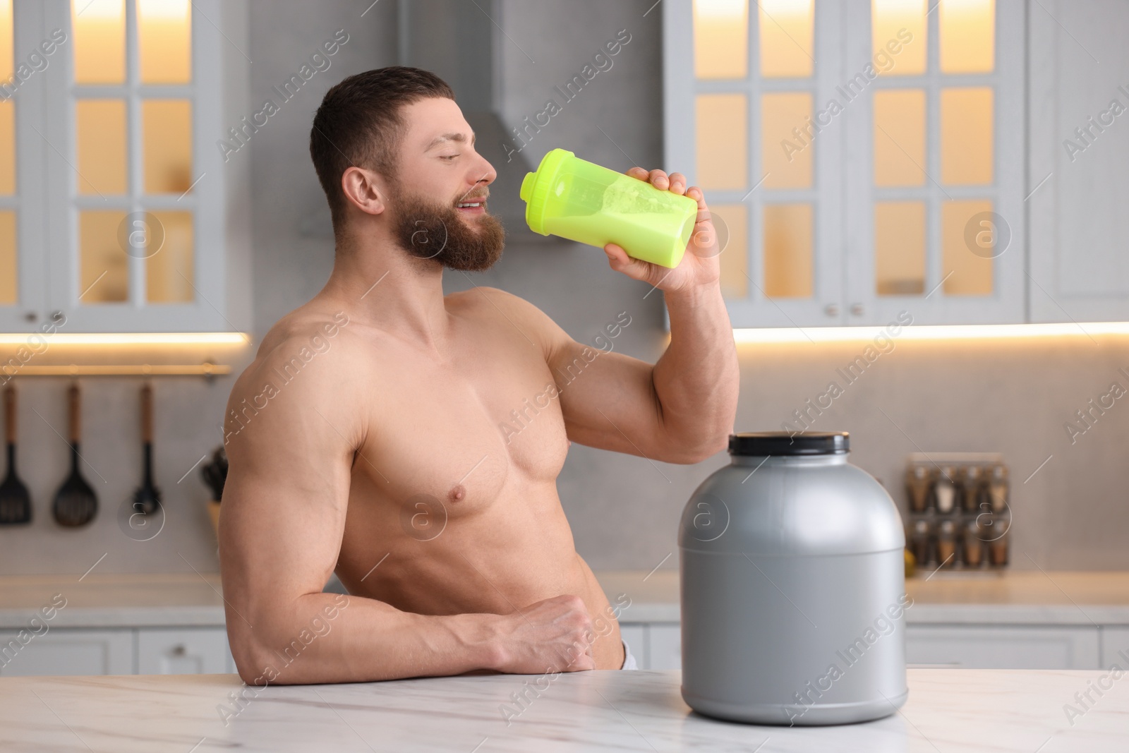 Photo of Young man with shaker of protein and powder at white marble table in kitchen