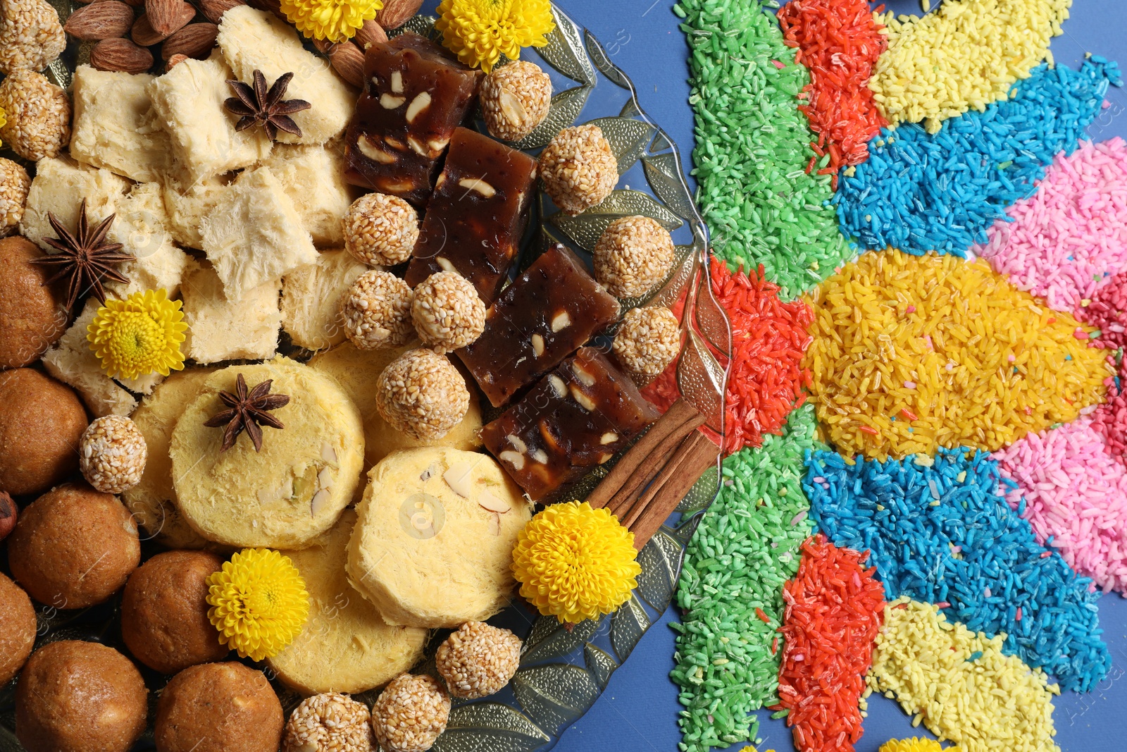 Photo of Diwali celebration. Tasty Indian sweets, spices, nuts and colorful rangoli on blue table, flat lay