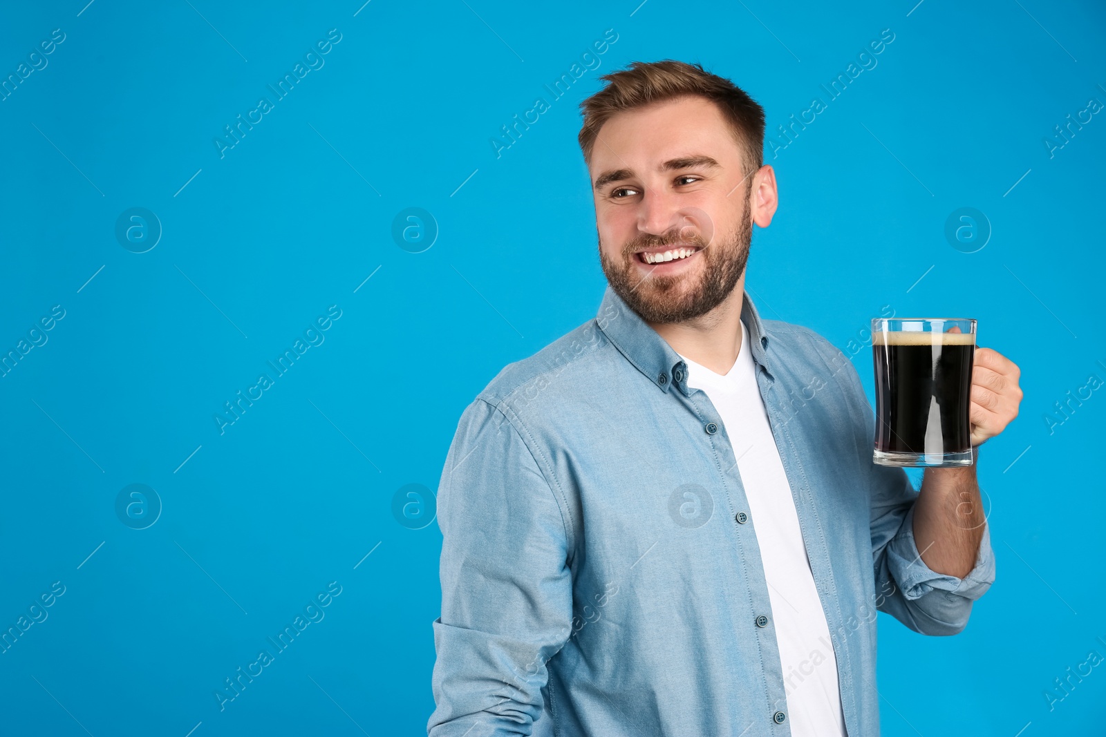 Photo of Handsome man with cold kvass on blue background. Traditional Russian summer drink