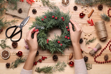 Photo of Florist making beautiful Christmas wreath with berries at wooden table, top view
