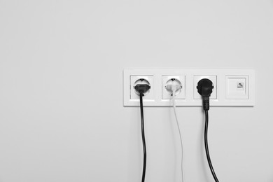 Power sockets with inserted plugs on white wall, space for text. Electrical supply