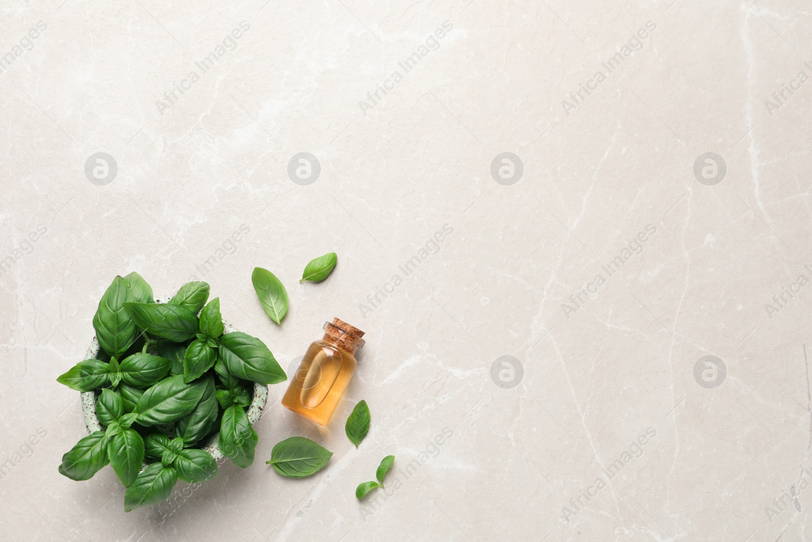 Photo of Bottle of essential basil oil and fresh leaves on light marble table, flat lay. Space for text