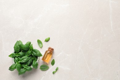 Photo of Bottle of essential basil oil and fresh leaves on light marble table, flat lay. Space for text